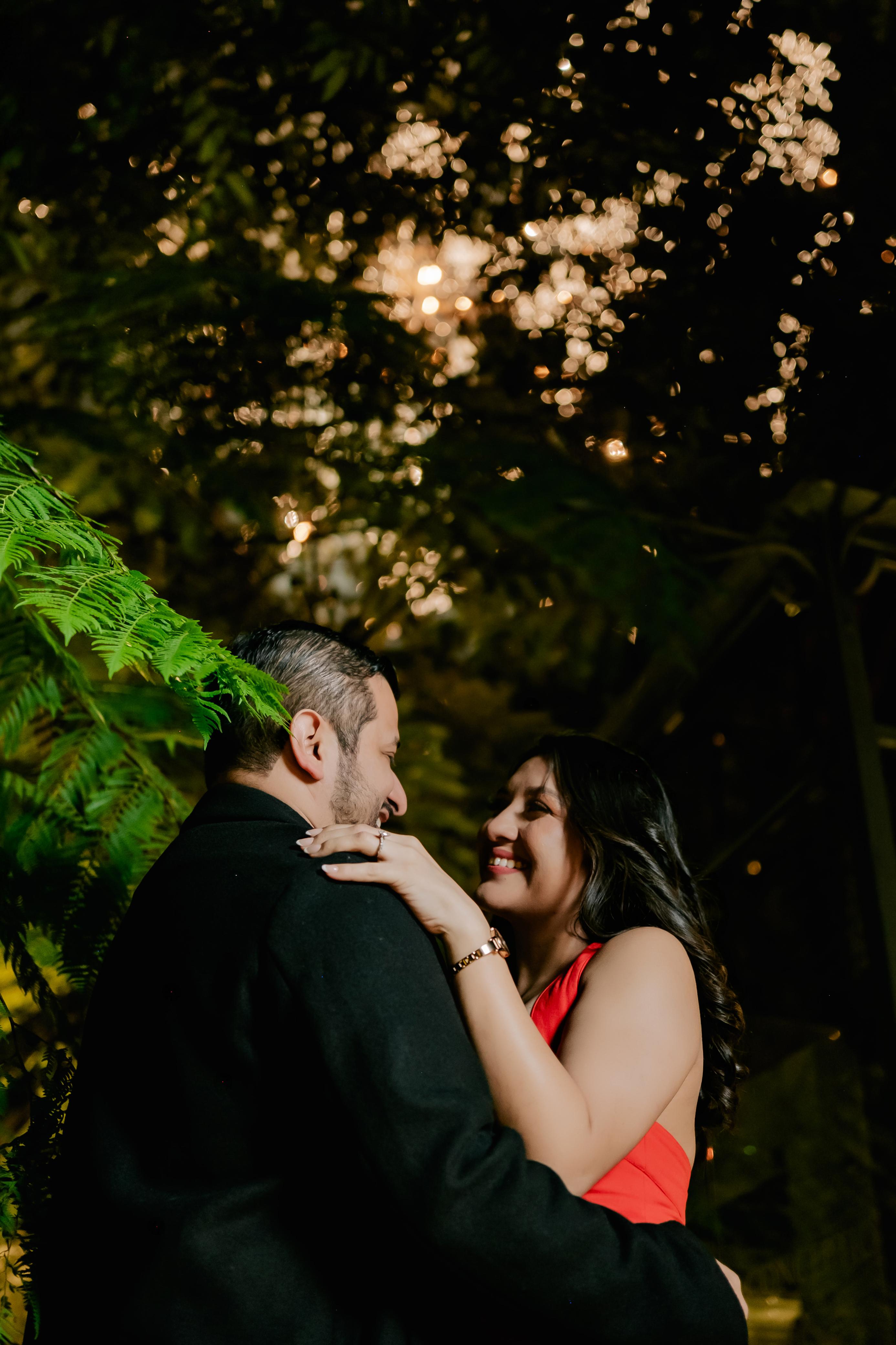 Daniela y Ariel sonriendo y abrazados entre jardines y luces